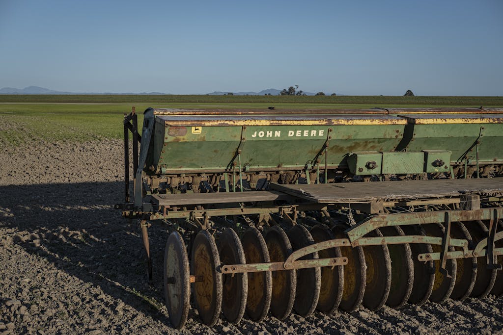 A John Deere seeder stands ready in a vast open field during the daytime.